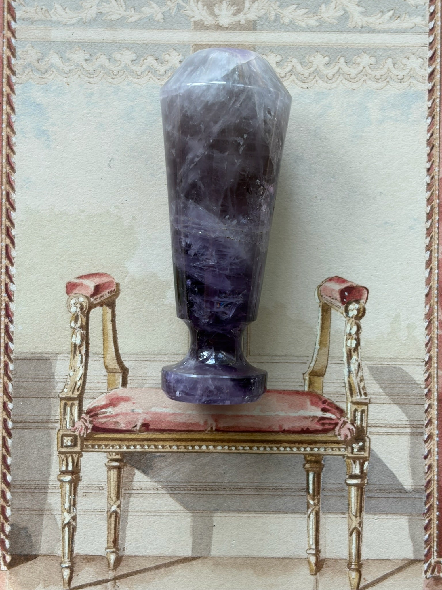 Faceted amethyst wax seal stamp displayed upright on a decorative chair, showing its full tapering shape