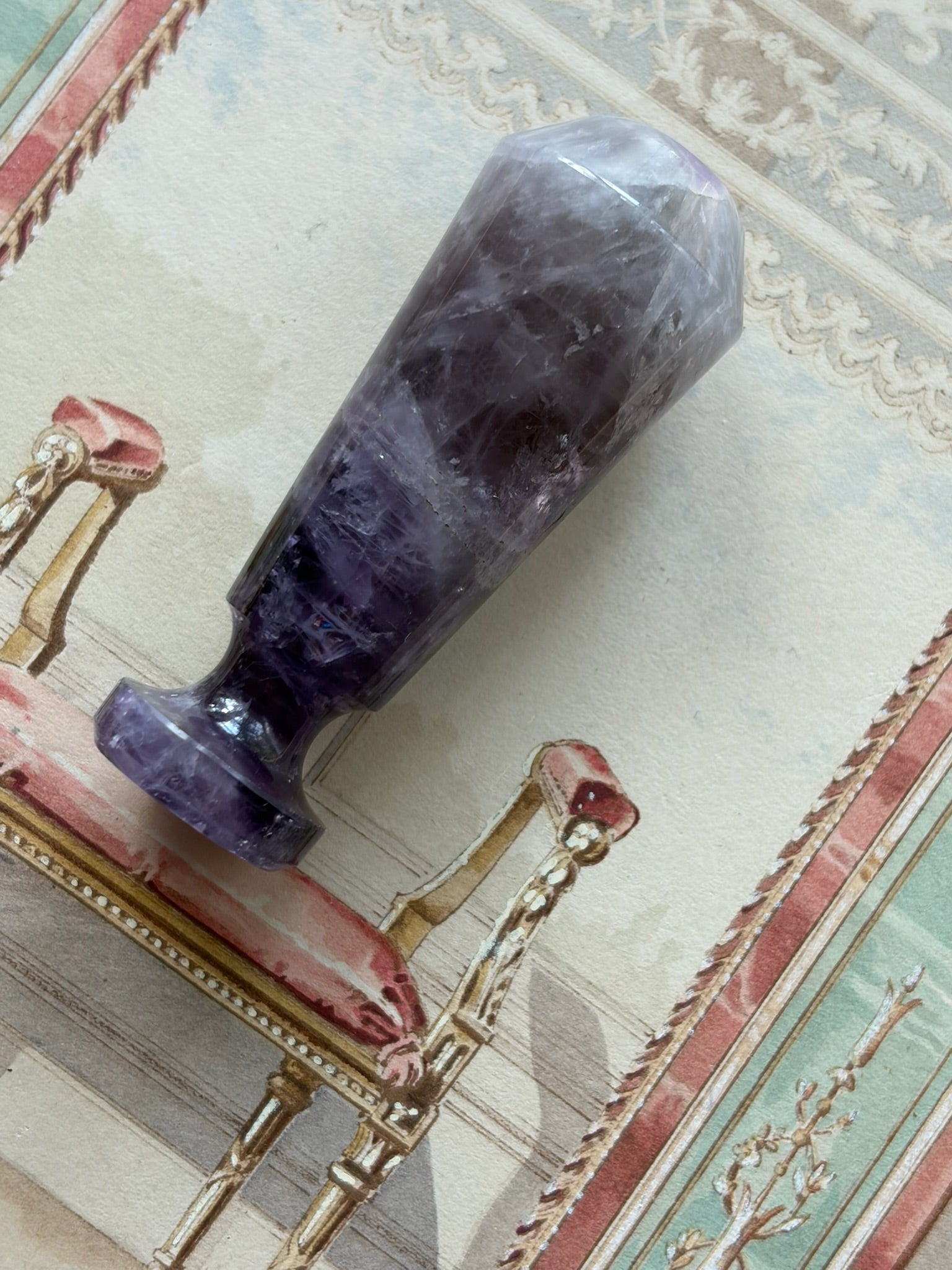 Faceted amethyst wax seal stamp with tapering polished shaft, resting on its side on a table