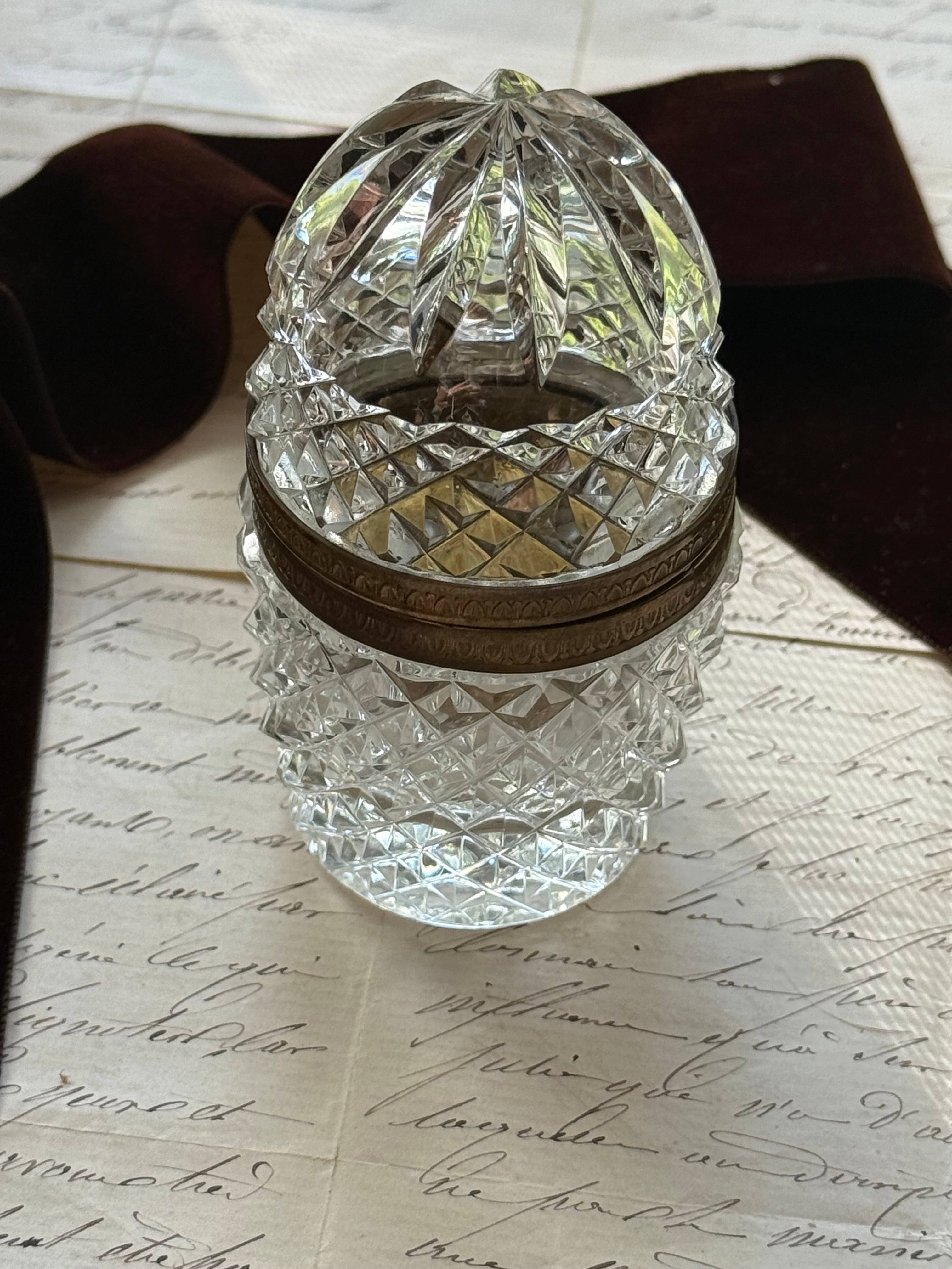 French crystal domed trinket box displayed beside a velvet ribbon on antique script pages, showing the diamond-cut base and gilt band